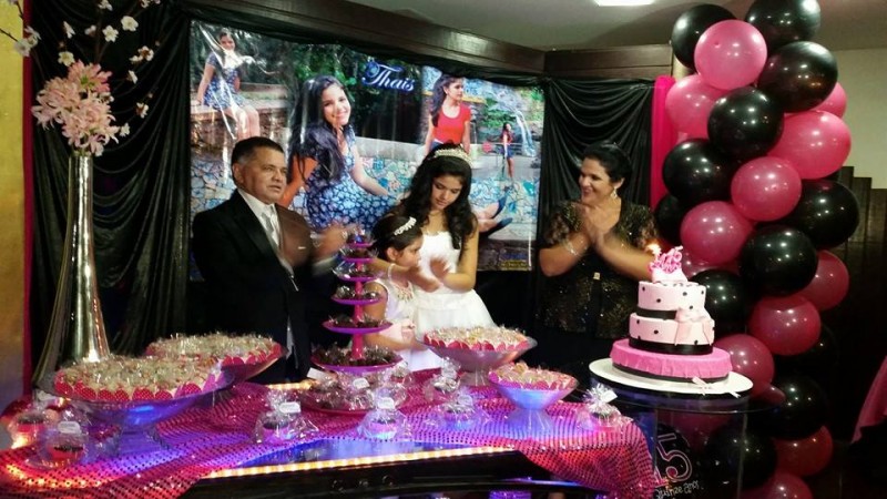 foto da debutante Thais com seus pais e irmã na mesa do bolo